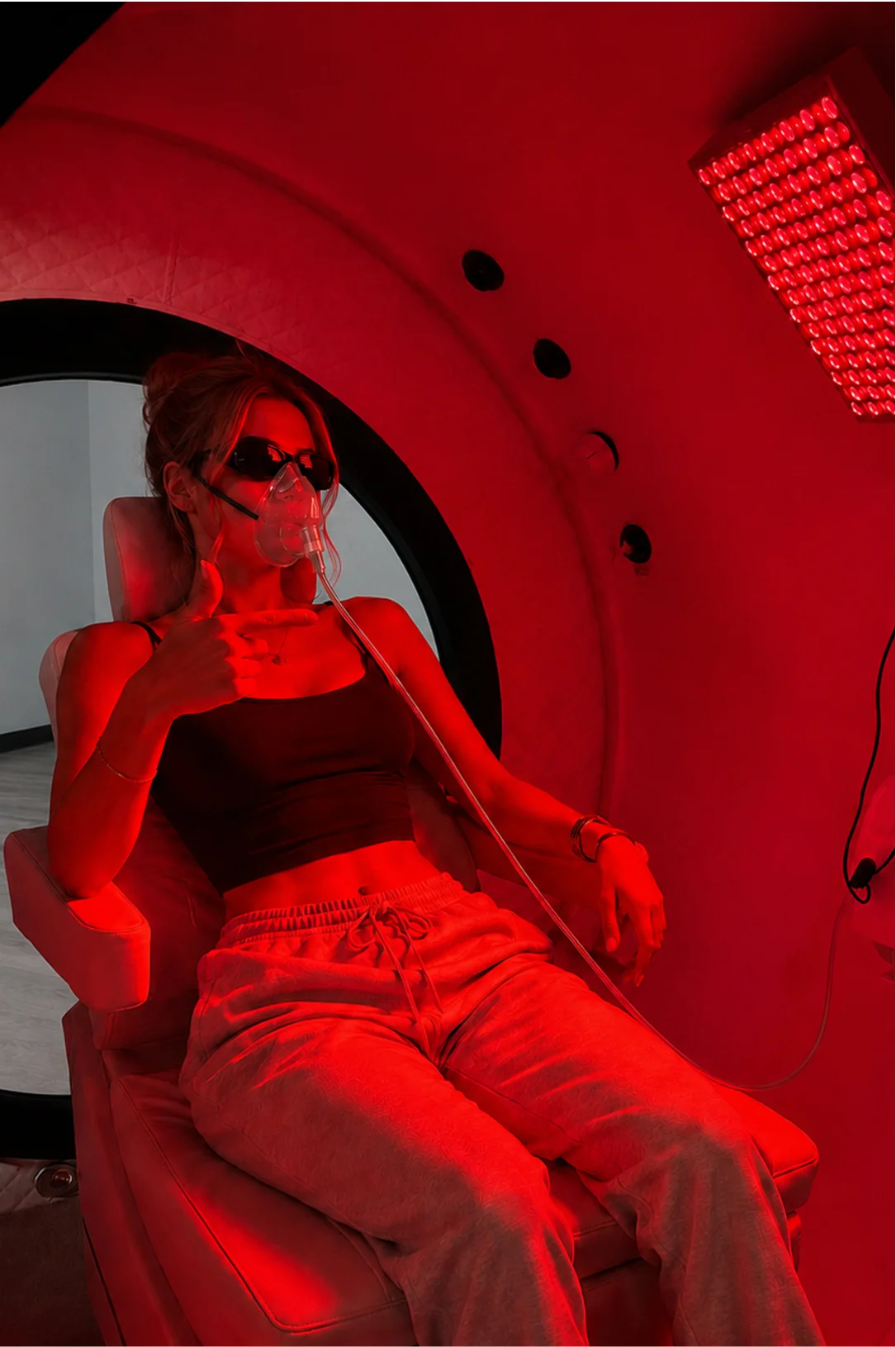 A guest reclining on oxygen inside a chamber, lit by the in-chamber red light panel